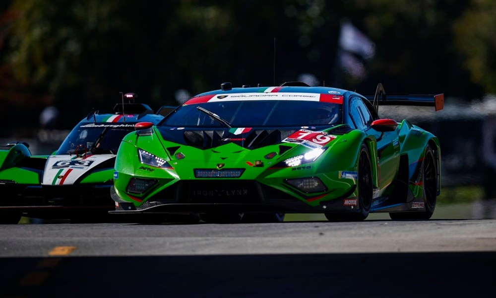 Two green IMSA cars racing trackside