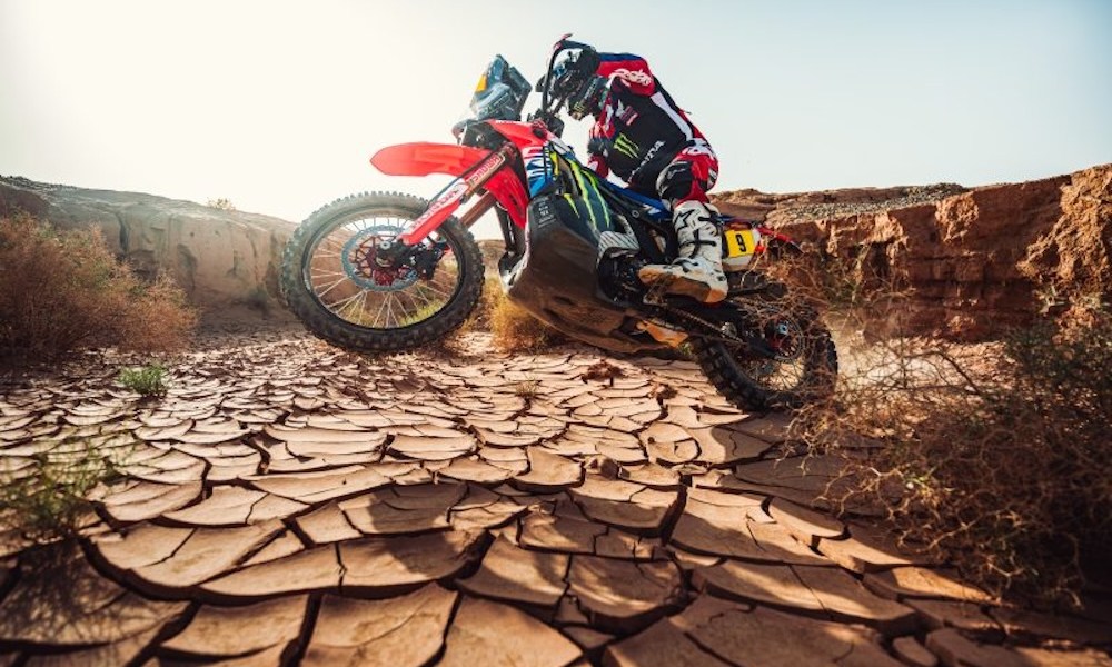 Motorcyclist crossing cracked desert terrain