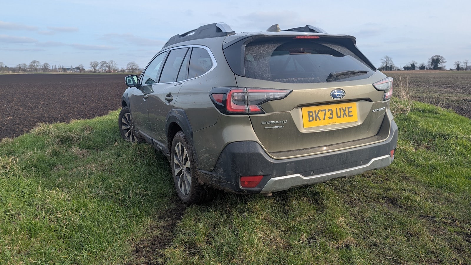 Green Subaru Outback parked in field